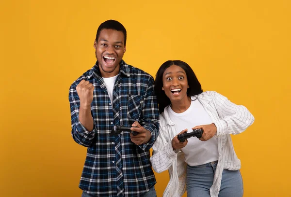 アフリカ系アメリカ人の若いカップルは成功の感情を表現し、オンラインゲームでジョイスティックで遊ぶ — ストック写真
