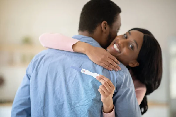 Millennial balck pareja emocionada por los resultados positivos de la prueba de embarazo, abrazándose en casa — Foto de Stock