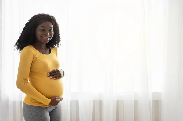 Hermosa mujer africana embarazada abrazando su gran vientre en casa — Foto de Stock