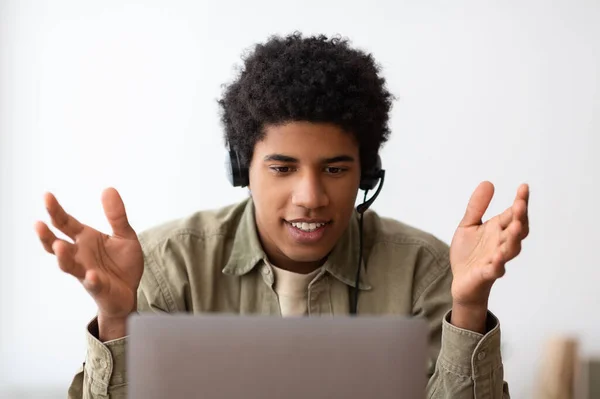 Conceito de educação baseado na Web. Feliz adolescente negro estudante em fone de ouvido conversando com seu professor universitário on-line no laptop, dentro de casa — Fotografia de Stock