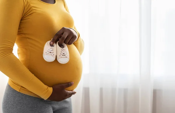 Primo piano di scarpe per bambini sulla pancia della signora nera incinta — Foto Stock