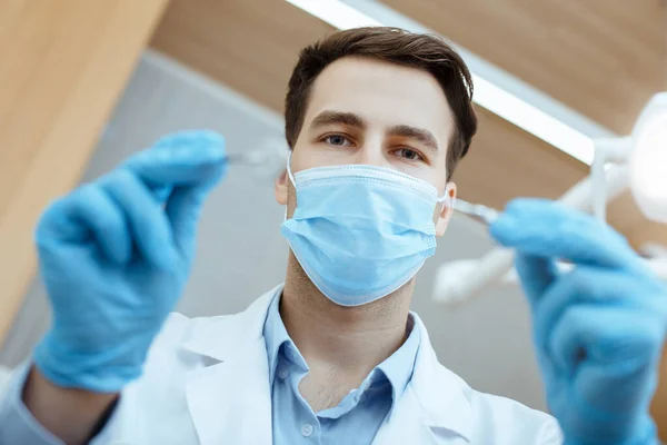 Joven dentista atractivo en abrigo blanco, máscara protectora y guantes de goma trata los dientes al paciente —  Fotos de Stock