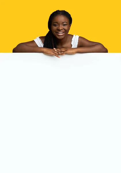 Plaats voor uw advertentie. Vreugdevolle zwarte vrouw leunend op blanco witte reclamebord — Stockfoto