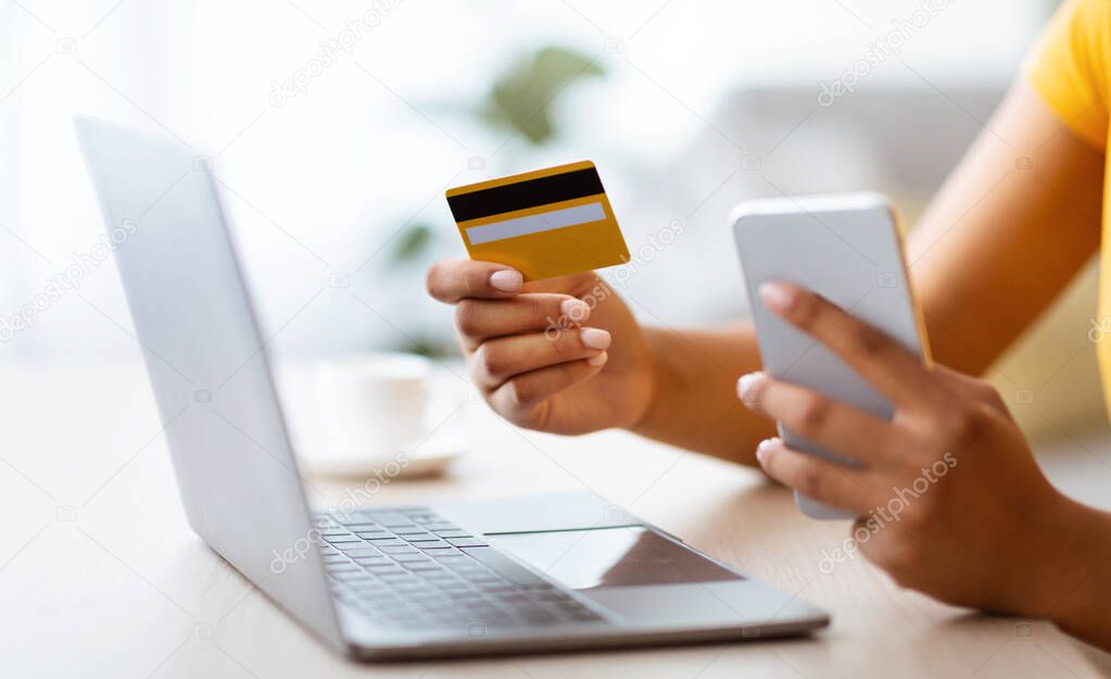 Black woman using smartphone and credit card sitting at desk