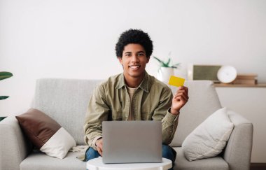 İnternet alışverişi. Bilgisayarın önünde kredi kartı gösteren, evden sipariş veren, pozitif siyah bir genç var.