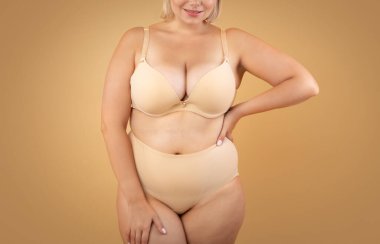 Kendini kabullenme. Bej arkaplanda iç çamaşırlı güzel kadın pozu