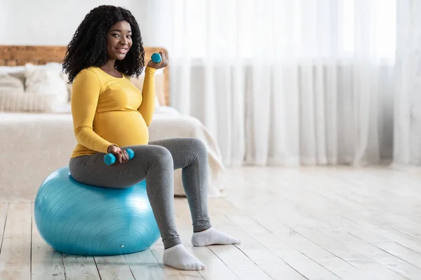 Усміхнена вагітна леді займається з барбеллами, сидячи на м'ячі — стокове фото