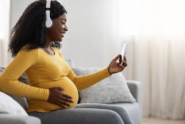 Senhora negra grávida desfrutando de música, usando o aplicativo móvel — Fotografia de Stock
