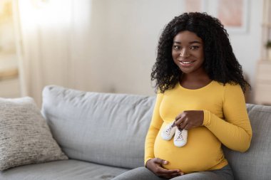 Karnında bebek ayakkabıları taşıyan neşeli hamile kadın.