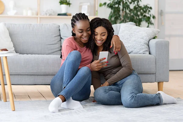 Duas irmãs africanas americanas alegres verificando as mídias sociais no smartphone — Fotografia de Stock