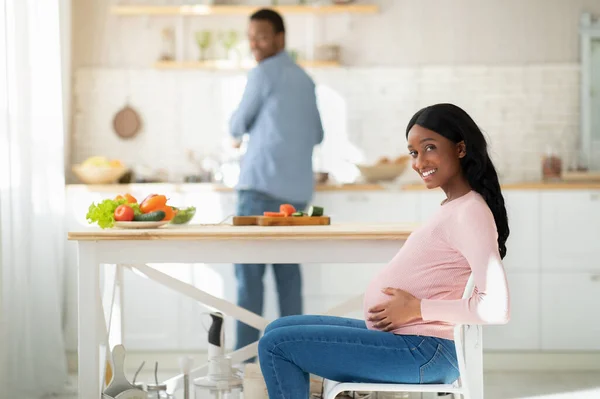 Hälsosam kost under graviditeten. Härligt förväntansfull kvinna väntar på sin man att laga hälsosam frukost i köket — Stockfoto