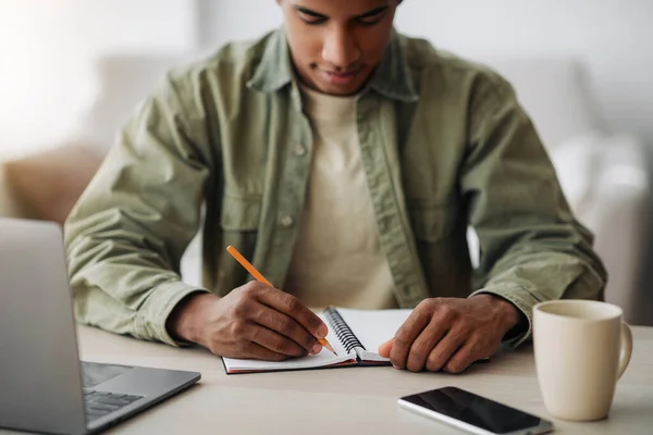 Concepto de aprendizaje remoto. Estudiante negro escribiendo en cuaderno durante la lección en línea en casa, se centran en las manos — Foto de Stock