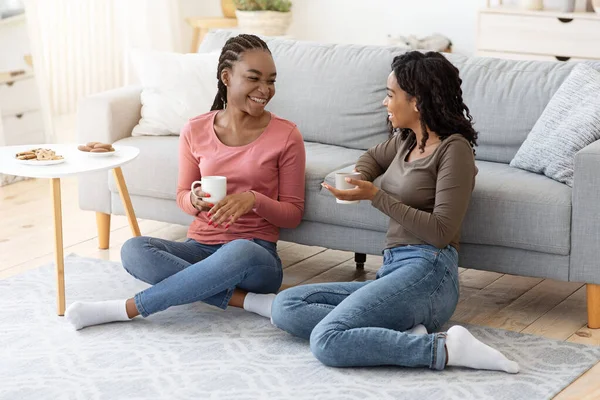 Feliz negro novias disfrutando fin de semana juntos, beber café en sofá — Foto de Stock