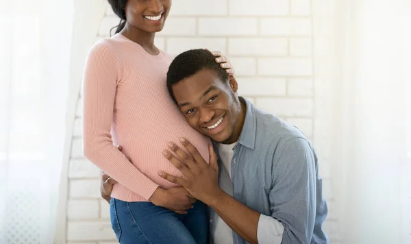 Любящий черный парень слушает своих подружек беременный животик дома, панораму — стоковое фото