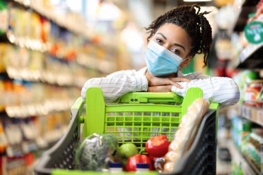 Süpermarkette içi yiyecek dolu alışveriş arabasıyla poz veren kadın