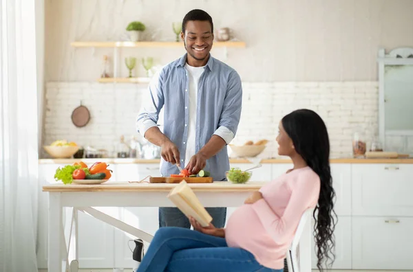 Feliz hombre negro haciendo ensalada de verduras frescas para su esposa embarazada en la cocina — Foto de Stock