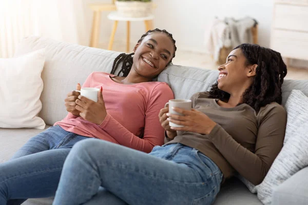 Avslappnade svarta damer dricka te, prata medan vila på soffan — Stockfoto