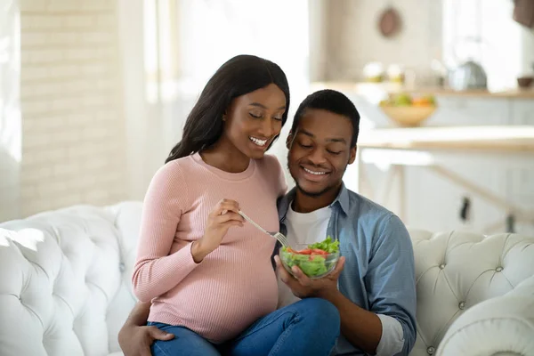 Nutrição saudável durante a gravidez. Esposo negro positivo e sua esposa expectante comendo salada de legumes frescos em casa — Fotografia de Stock