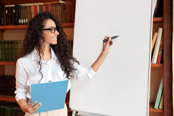 Mosolygó nő szemüvegben pózol közel üres flipchart — Stock Fotó