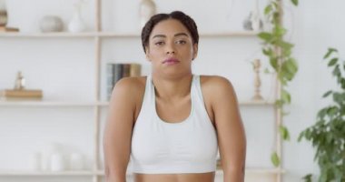 Genç Afro-Amerikan bayan sporcu evde omuzlarını ısıtıyor, kameraya bakıyor, yavaş çekimde.