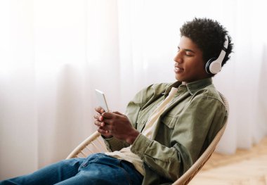 Evde cep telefonundan müzik listesi seçen kulaklı çekici siyahi bir genç.