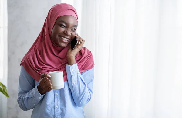 Smiling Black Muslim Lady Relaxing Near Window With Cellphone And Coffee — Stock Photo, Image