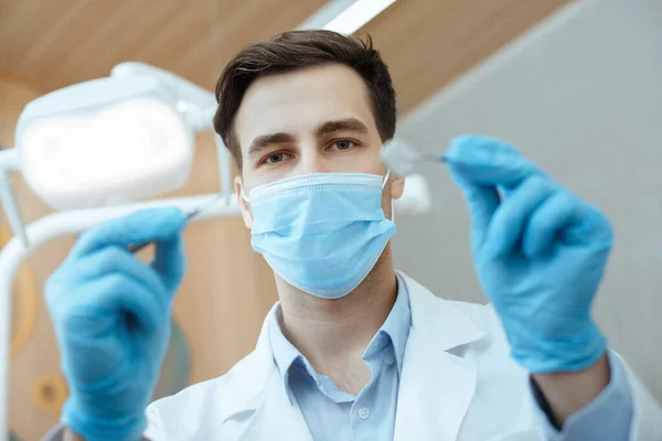 Professionele mannelijke tandarts in witte jas, beschermend masker en handschoenen houden tandheelkundige instrumenten en start baan — Stockfoto