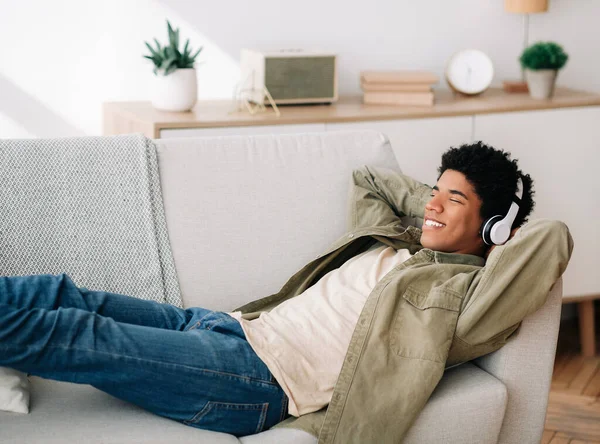 Glad svart tonåring kille i hörlurar liggande på bekväm soffa och lyssna på musik hemma, kopiera utrymme — Stockfoto