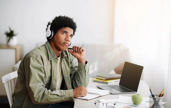 Pensive zwarte tiener in koptelefoon passeren moeilijke examen op laptop, denken over zijn antwoord thuis, ruimte voor design — Stockfoto