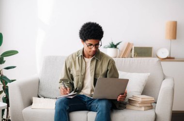 Uzaktan öğrenme konsepti. Çalışkan genç öğrenci dizüstü bilgisayarı ile evde çevrimiçi ders sırasında not alıyor.