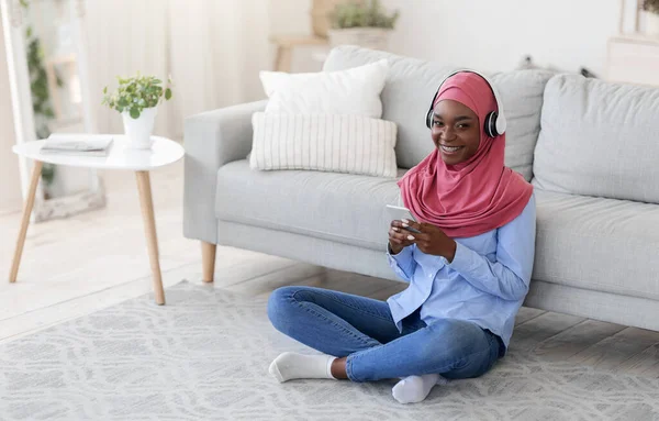 Tinggallah di rumah. Smiling Black Muslim Woman Relaxing With Smartphone And Headphones — Stok Foto