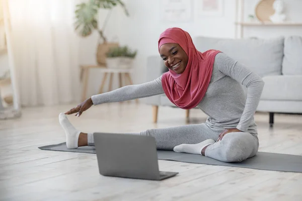 Svart muslimsk kvinna i hijab tränar framför laptop hemma — Stockfoto