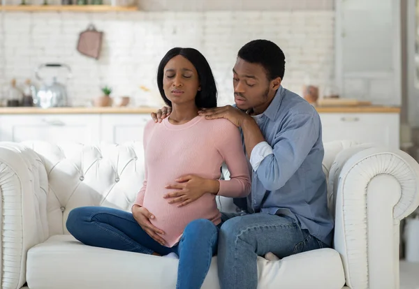 Занепокоєний чорний чоловік, що підтримує вагітну дружину з пренатальними скороченнями вдома — стокове фото