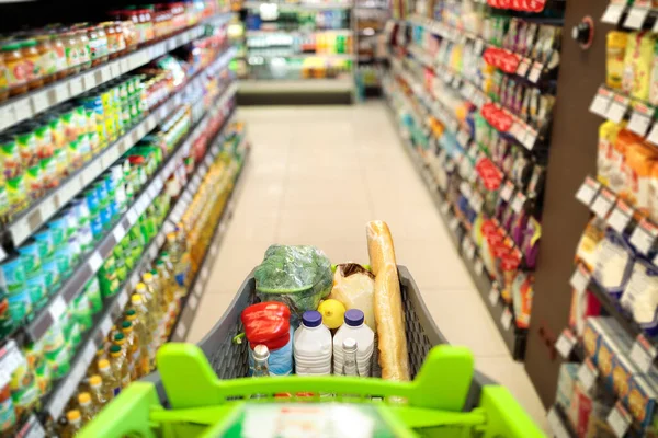 Shopping Cart Full Of Food Products Over Supermarket Aisle Background — Stock Photo, Image