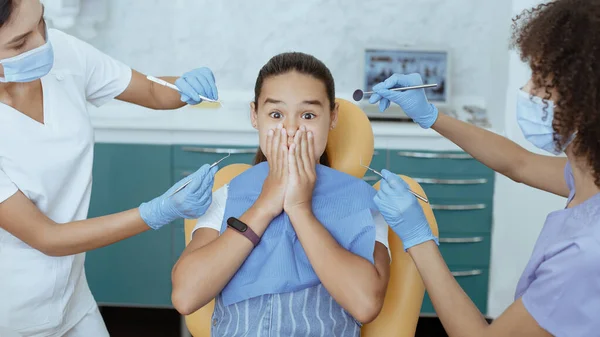 Piccola ragazza latina con gli occhi spalancati copre la bocca con le mani e impedisce ai medici di trattare i denti — Foto Stock