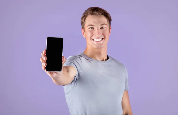 Jovem desportista feliz mostrando smartphone com tela vazia sobre fundo lilás, mockup para design de aplicativo móvel — Fotografia de Stock