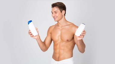 Elinde şampuan şişeleriyle duran yakışıklı genç adam.