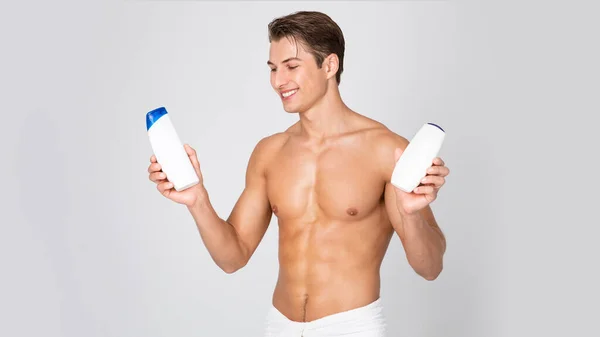 Guapo joven de pie con botellas de champú en las manos — Foto de Stock