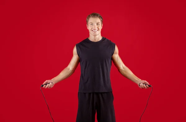Konsep latihan kardio. Pemuda fit olahragawan melompat-lompat tali di atas latar belakang studio merah — Stok Foto