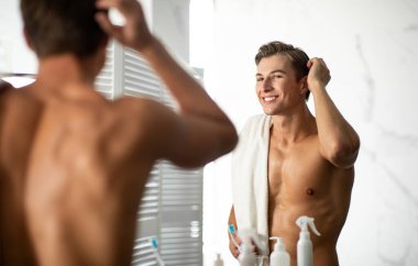 Yakışıklı genç adam elinde havluyla aynaya bakıyor.