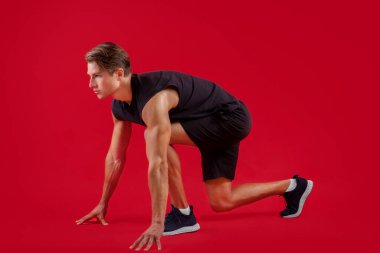 Güçlü milenyum sporcusu kırmızı stüdyo arka planı, yan bakış açısında başlangıç pozisyonunda.