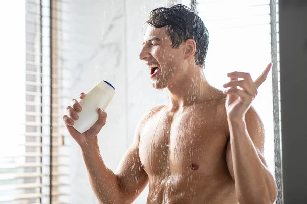 Schöner junger Mann wäscht Körper singend in Shampoo-Flasche — Stockfoto