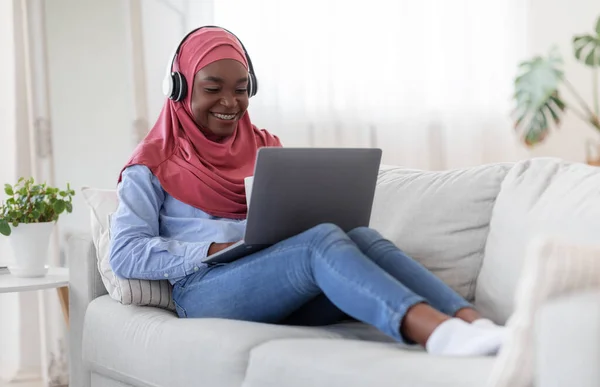 Disfrutando del tiempo en casa. Negro musulmana mujer usando el ordenador portátil y beber café — Foto de Stock