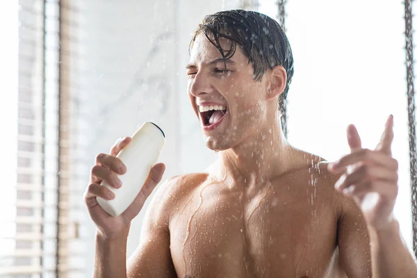 Junger Mann wäscht Körper singend in Shampoo-Flasche — Stockfoto
