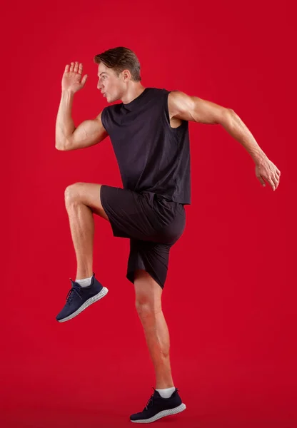 Zijaanzicht van de jonge mannelijke sprinter hardlopen, oefenen op rode studio achtergrond — Stockfoto