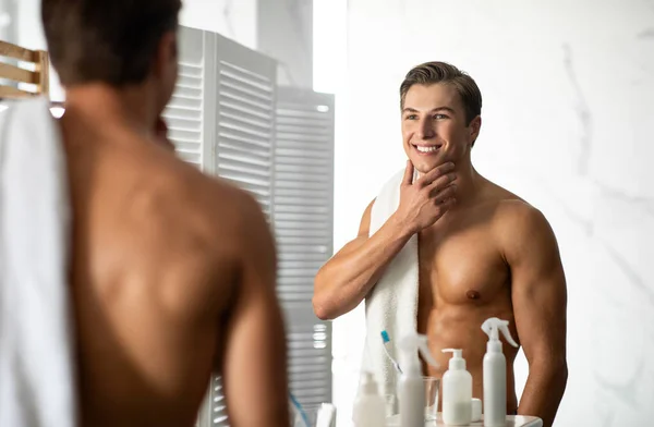 Selbstbewusster junger Mann blickt in den Spiegel, berührt Kinn — Stockfoto