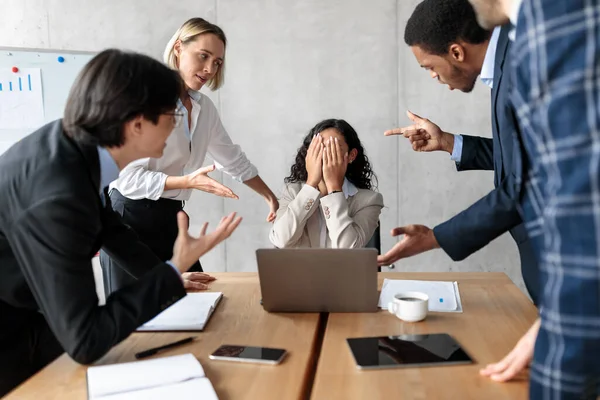 Unhappy Businesswoman Covering Face While Coworkers Shouting At Her Indoors