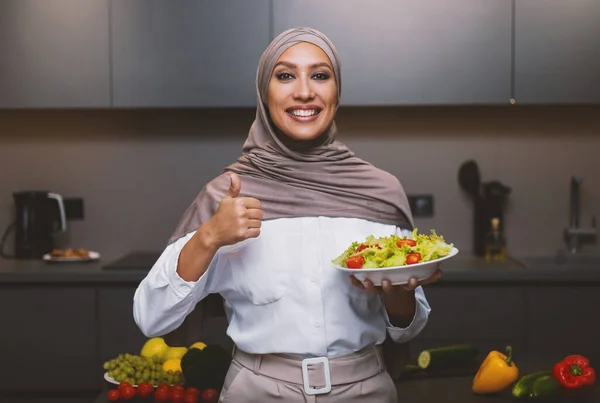 Arab nő gazdaság saláta Gesturing hüvelykujj-up jóváhagyó recept a konyhában — Stock Fotó
