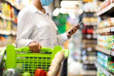 Cep telefonu kullanan tanınmayan Afrikalı Kadın süpermarketten alışveriş yapıyor.