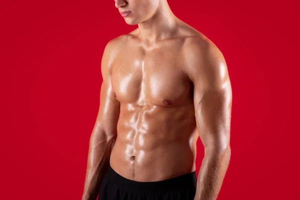 Kırmızı stüdyo arka planında çıplak gövdesi ve kasları olan genç ve güçlü sporcunun yakın görüntüsü. — Stok fotoğraf
